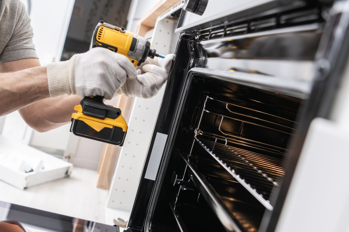 Technician repairing an oven with a power drill in San Leandro